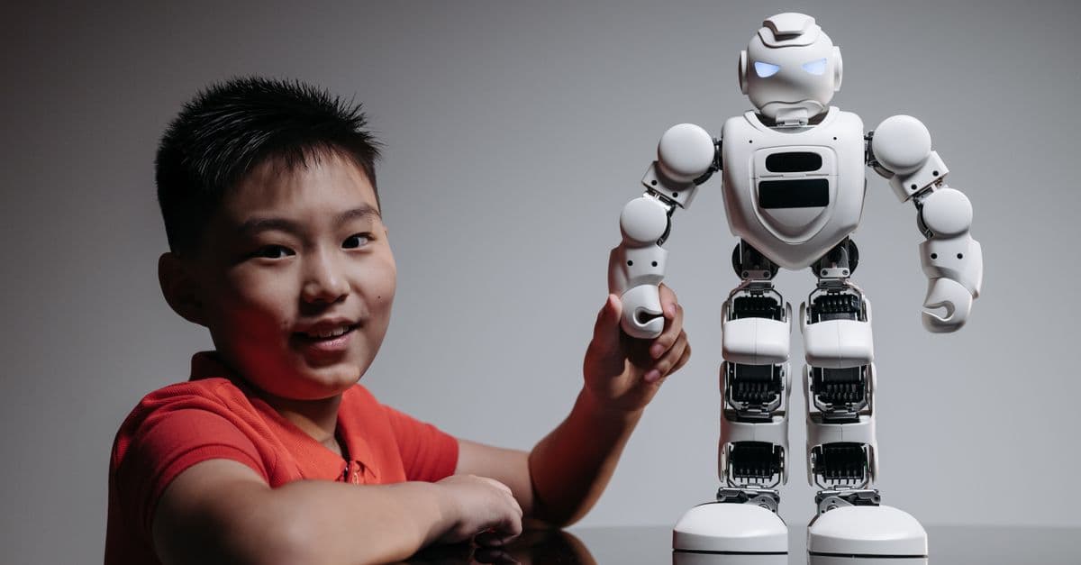 A young boy in a red shirt engaging with a humanoid robot indoors.