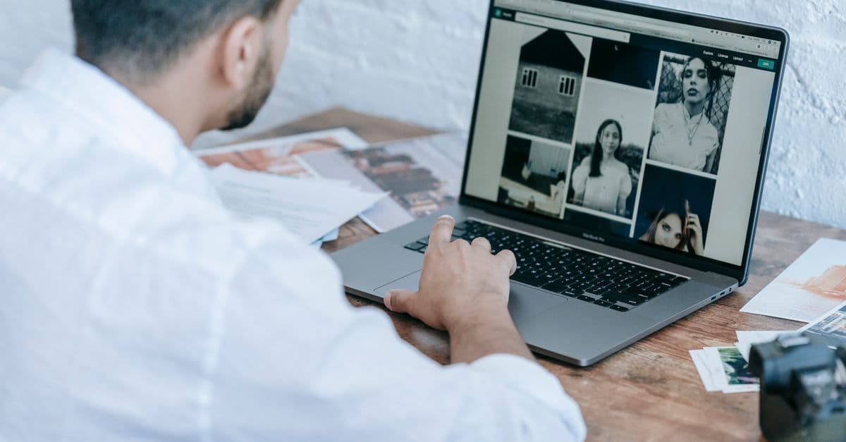 Side view of crop bearded male photographer using laptop while preparing pictures for publishing in modern workplace