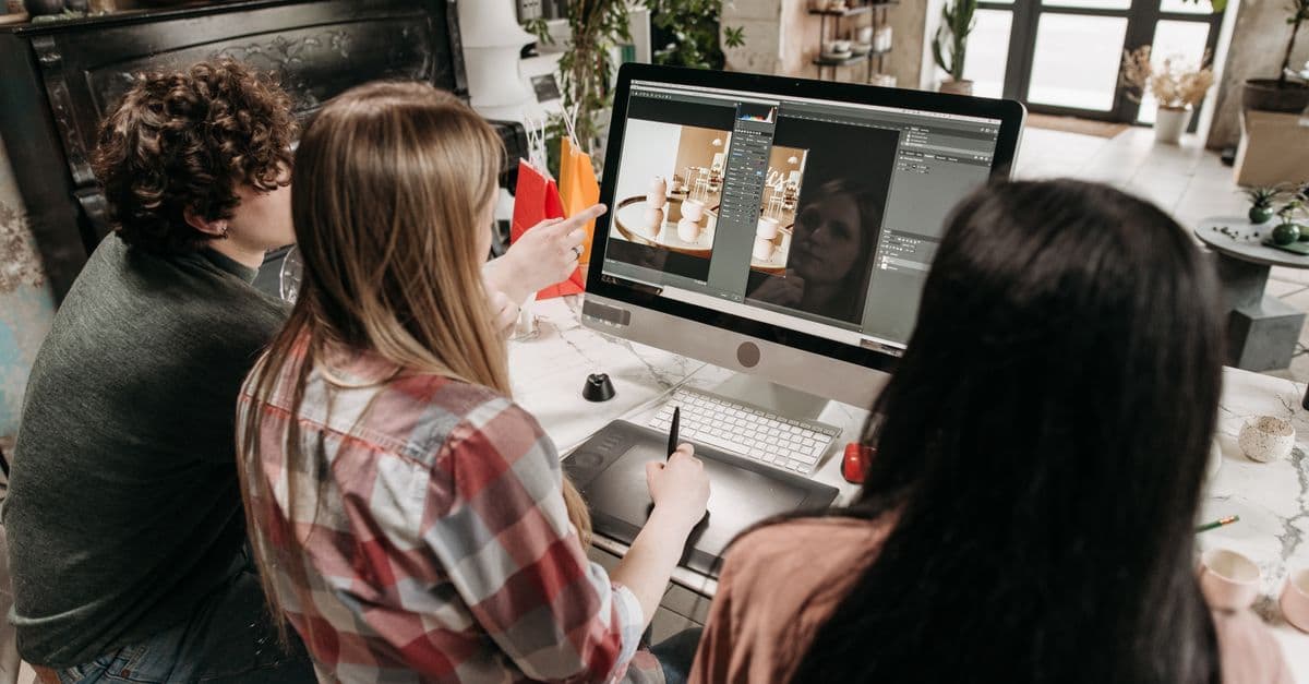A group of young adults working on a design project using a desktop computer in an artistic workspace.