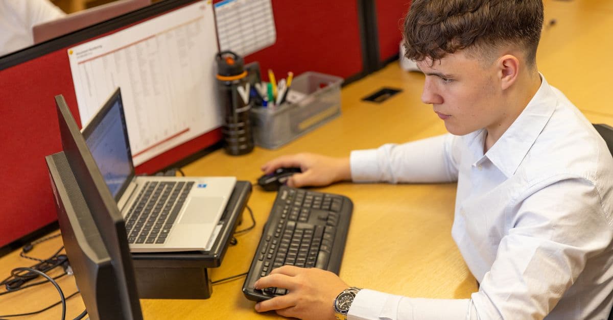Young male office worker engaged with computer tasks in a modern office setting.