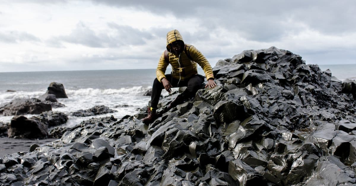 Person exploring rugged coastal rocks under cloudy skies by the sea.
