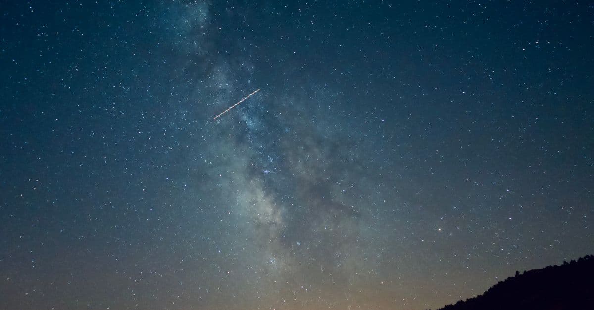 A breathtaking view of a starry sky featuring the Milky Way and a meteor streaking across.