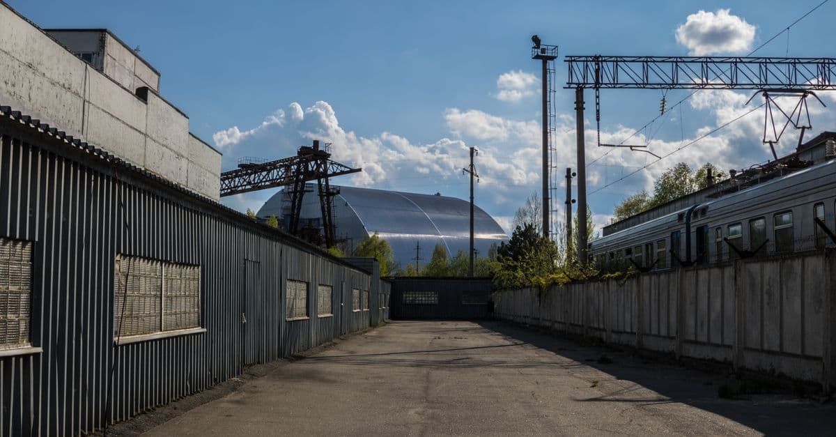 View of Chernobyl's new safe confinement and railway tracks under a blue sky.