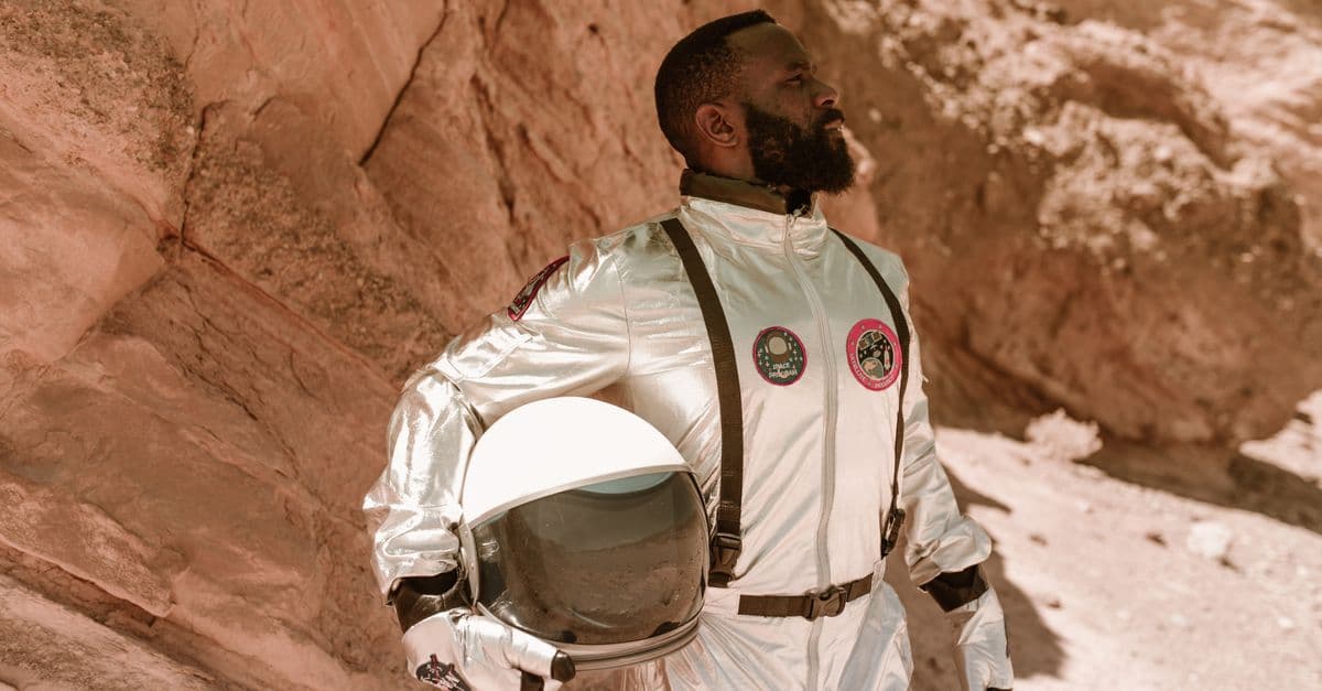 Young astronaut in a space suit posing with helmet in a desert terrain.
