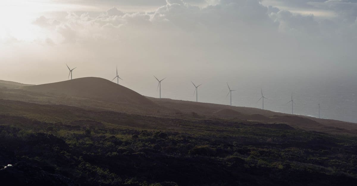 Wind turbines spin on hills under a cloudy sky, creating an eco-friendly energy source.