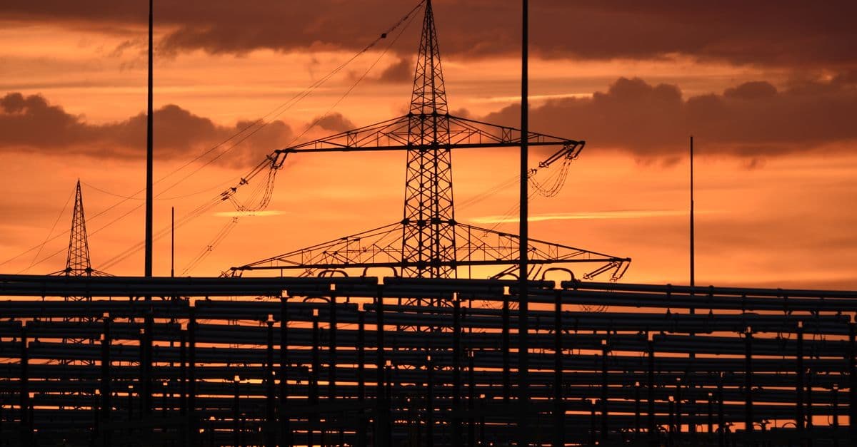 Silhouetted electric tower against vivid sunset sky, highlighting urban infrastructure.