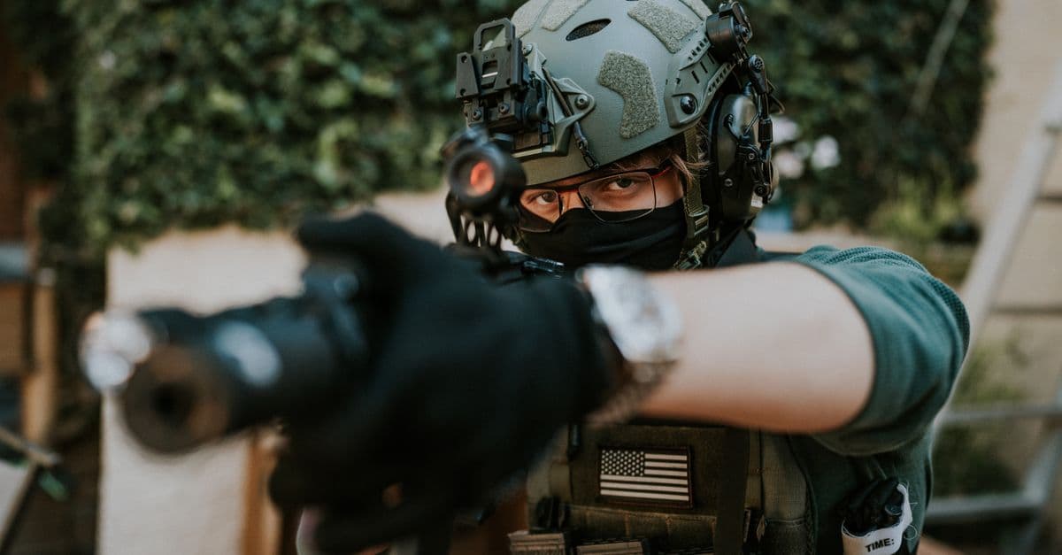 Soldier equipped with tactical gear and helmet in a ready stance outdoors.