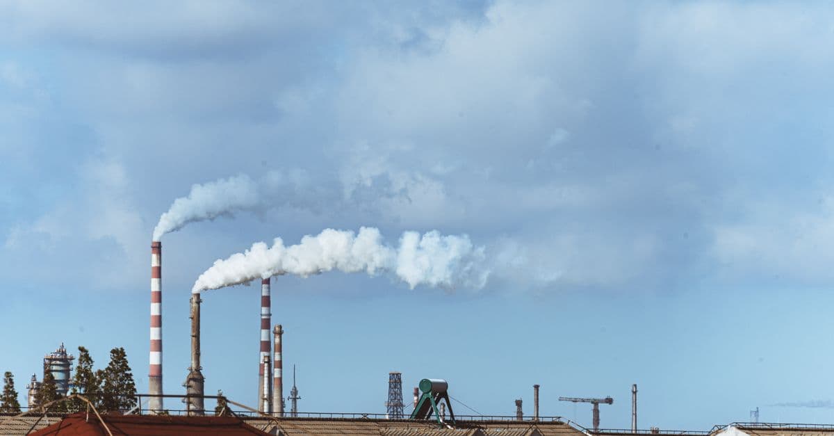 Factory chimneys emitting smoke over rooftops on a clear day, illustrating urban pollution.