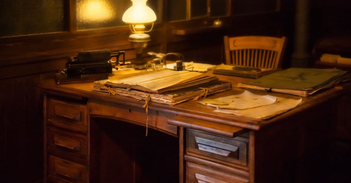 Cozy vintage office setting with an antique typewriter, lamp, and paperwork on a wooden desk.