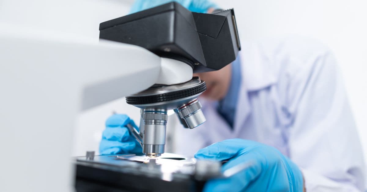 Close-up of a scientist examining samples under a microscope in a lab setting.