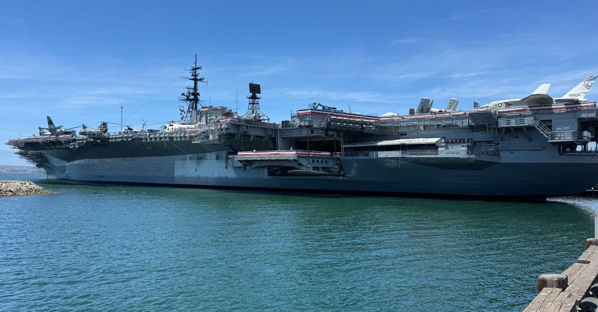 The USS Midway, a historic aircraft carrier, docked in the scenic San Diego Harbor, under clear blue skies.