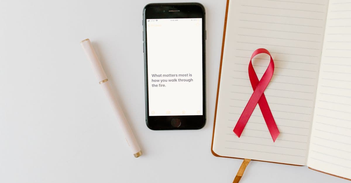 Pink ribbon symbolizing cancer awareness next to a notebook and smartphone on a white surface.