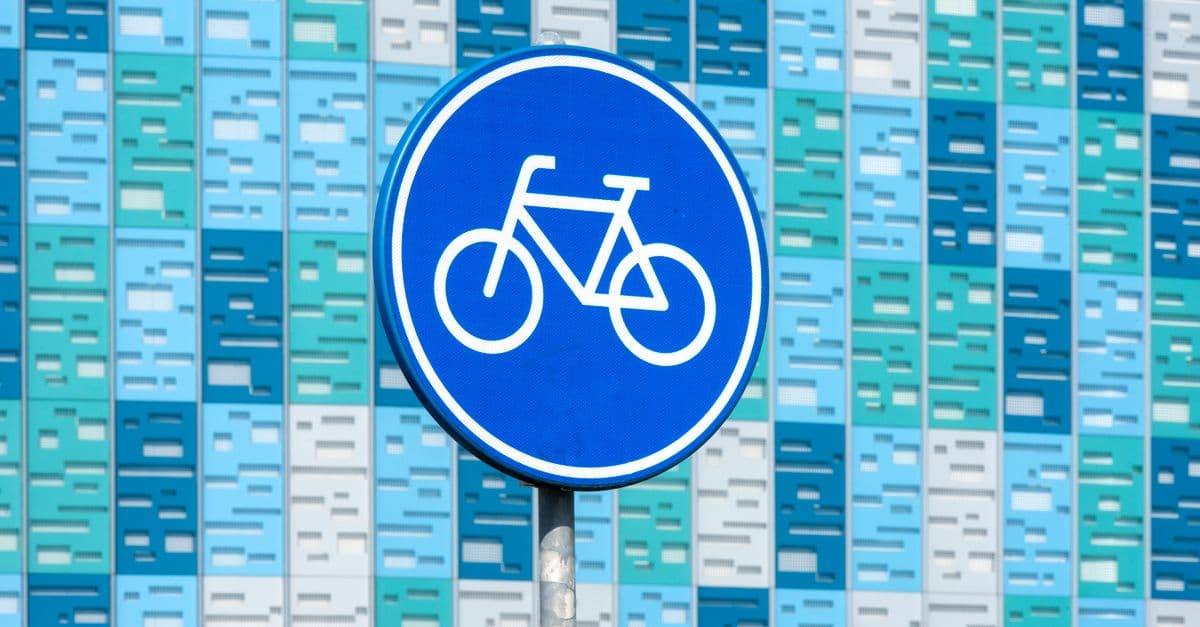 Bright blue bicycle sign in front of a modern geometric facade in various shades of blue.