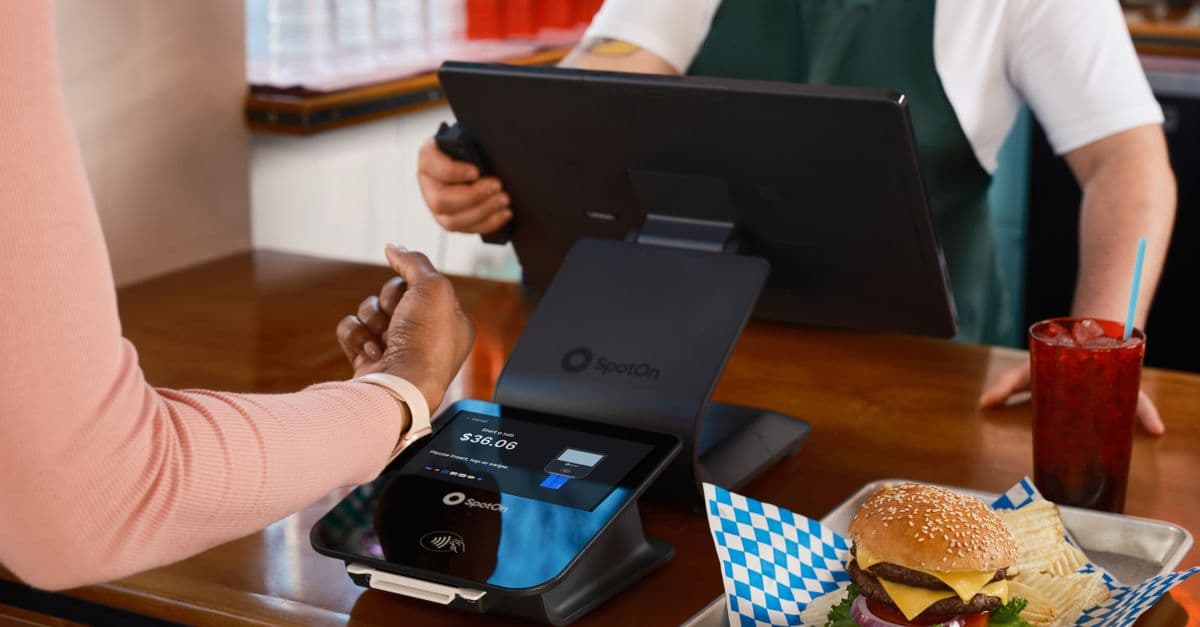 Customer using contactless payment at a restaurant counter with a burger and drink.