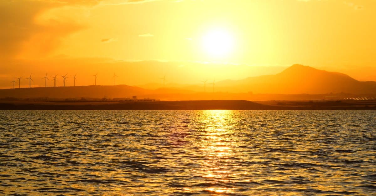 Stunning sunrise over Larnaca Bay with wind turbines and golden reflections on the water.