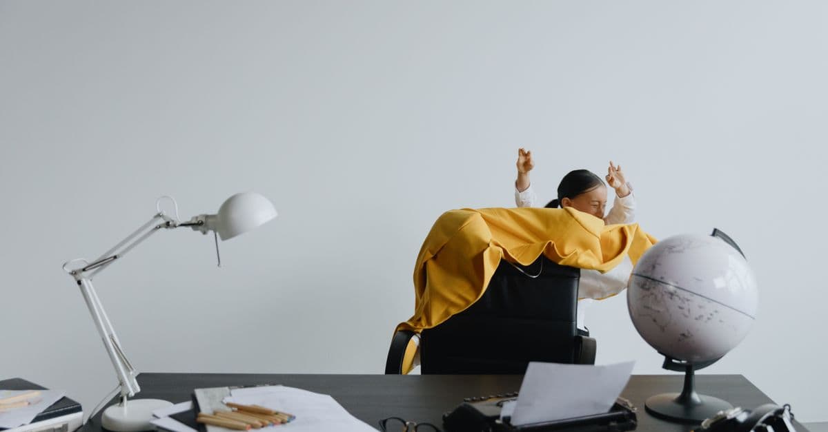 Child playing in office chair, surrounded by desk items and globe, creating a lively work atmosphere.