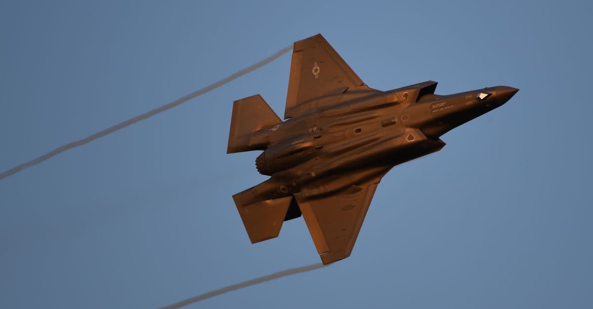 A dynamic shot of a military jet soaring through a clear blue sky during daylight.