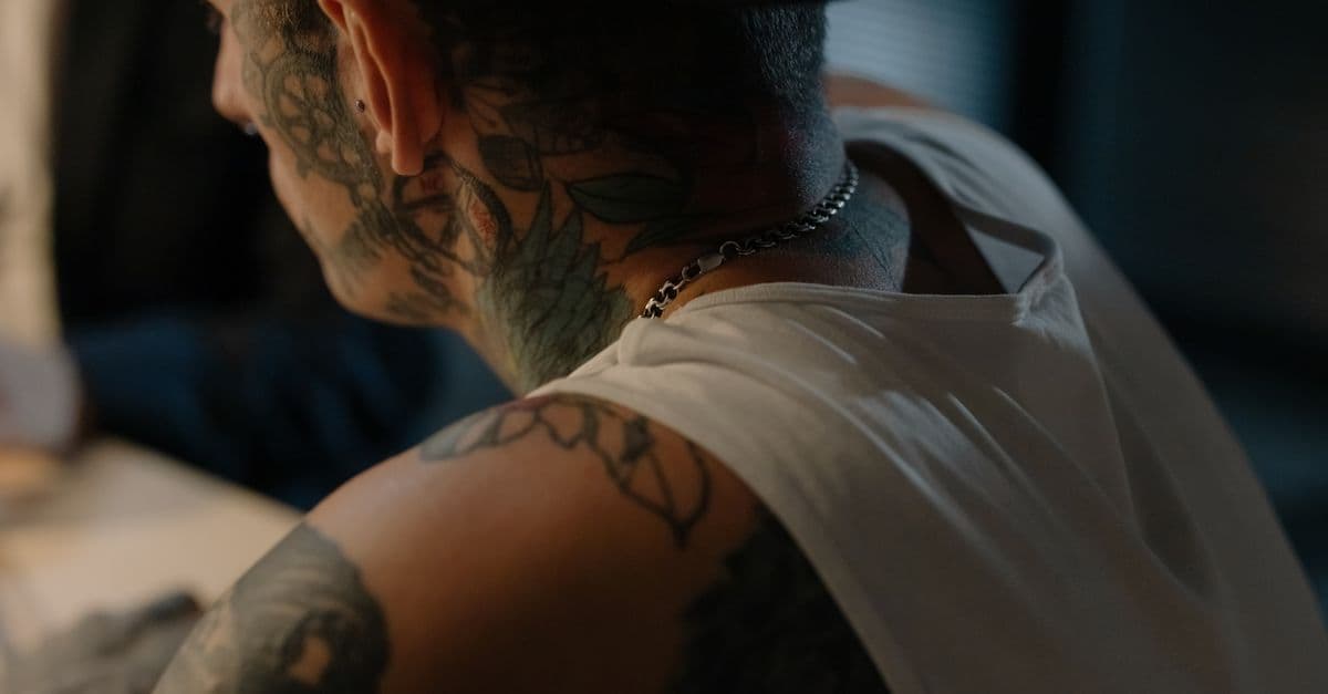 Close-up of a tattooed man in a tank top indoors, showcasing intricate body art.