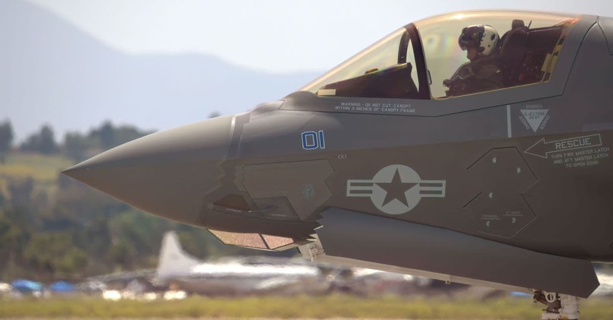 Close-up of a military fighter jet with pilot on a runway, equipped for action.