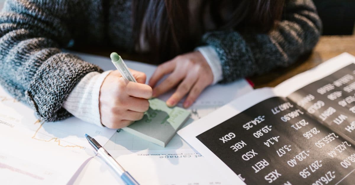 Close-up of a person writing on a sticky note amidst documents in an office setting.