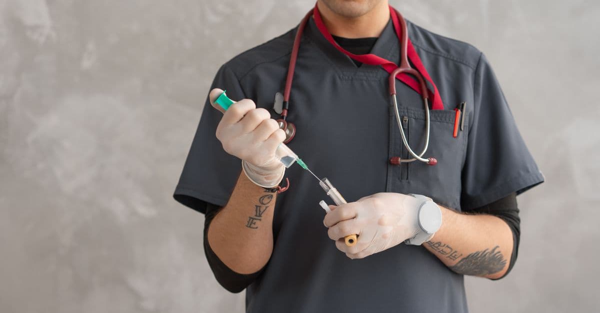 A healthcare worker in scrubs prepares a syringe with precision.