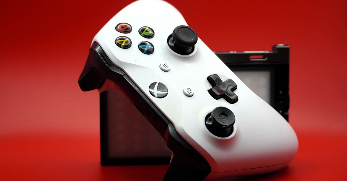 Close-up of a white gaming controller with black buttons against a vivid red backdrop.