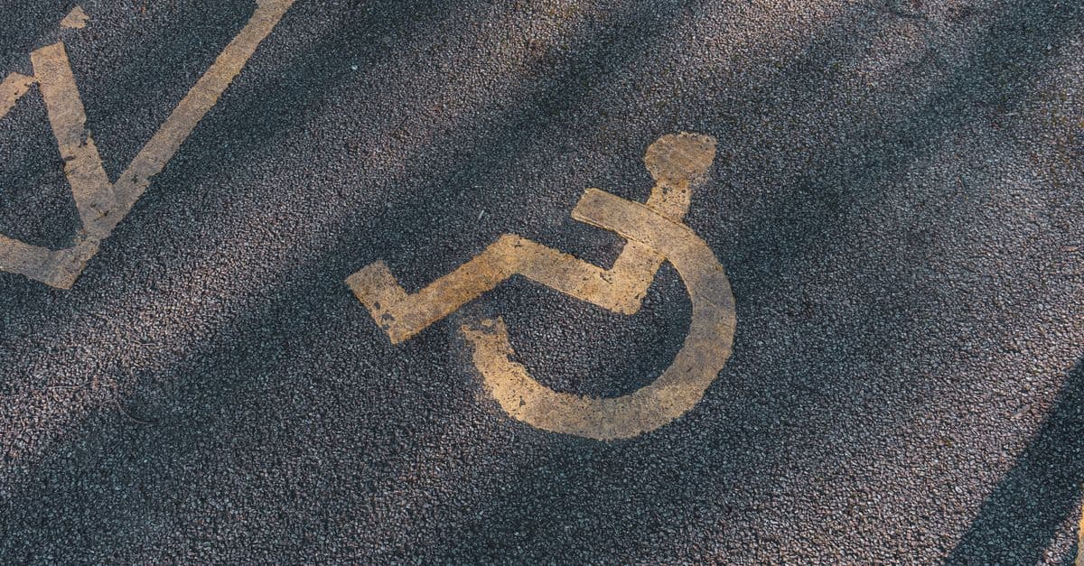 Close-up of an asphalt parking spot with a yellow wheelchair symbol for accessibility.
