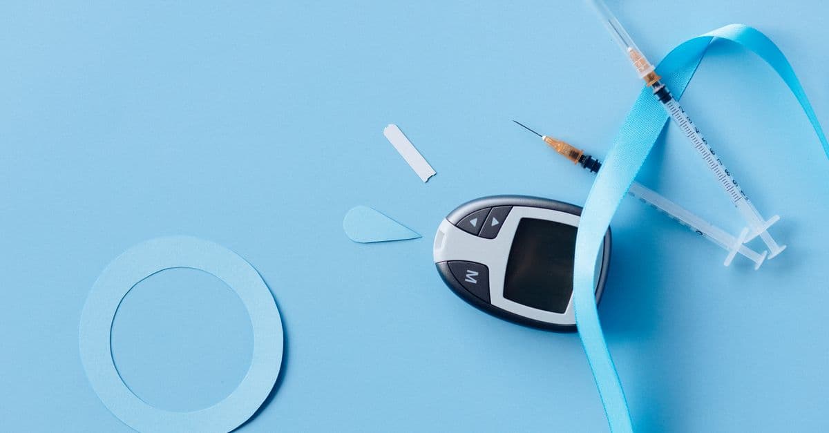 Flat lay of a diabetes monitoring kit with syringes and glucose meter on a blue background.