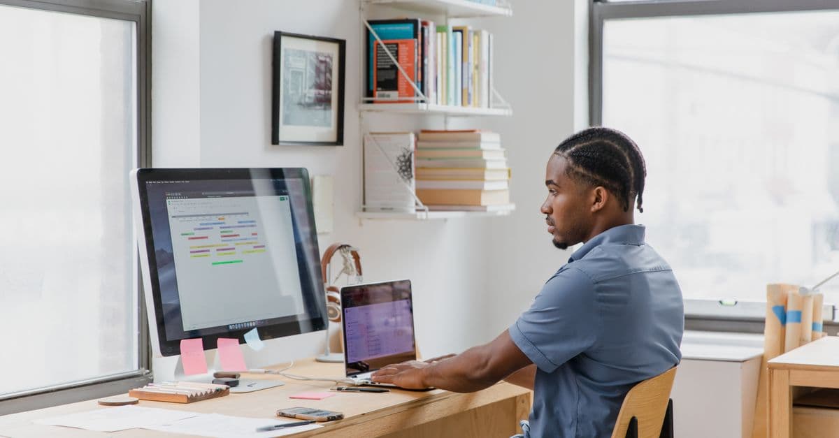 Focused man at home office desk working on dual screens. Ideal for remote work themes.