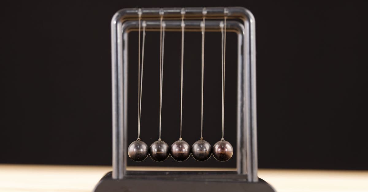 Close-up of a Newton's Cradle resting on a wooden surface against a dark background.
