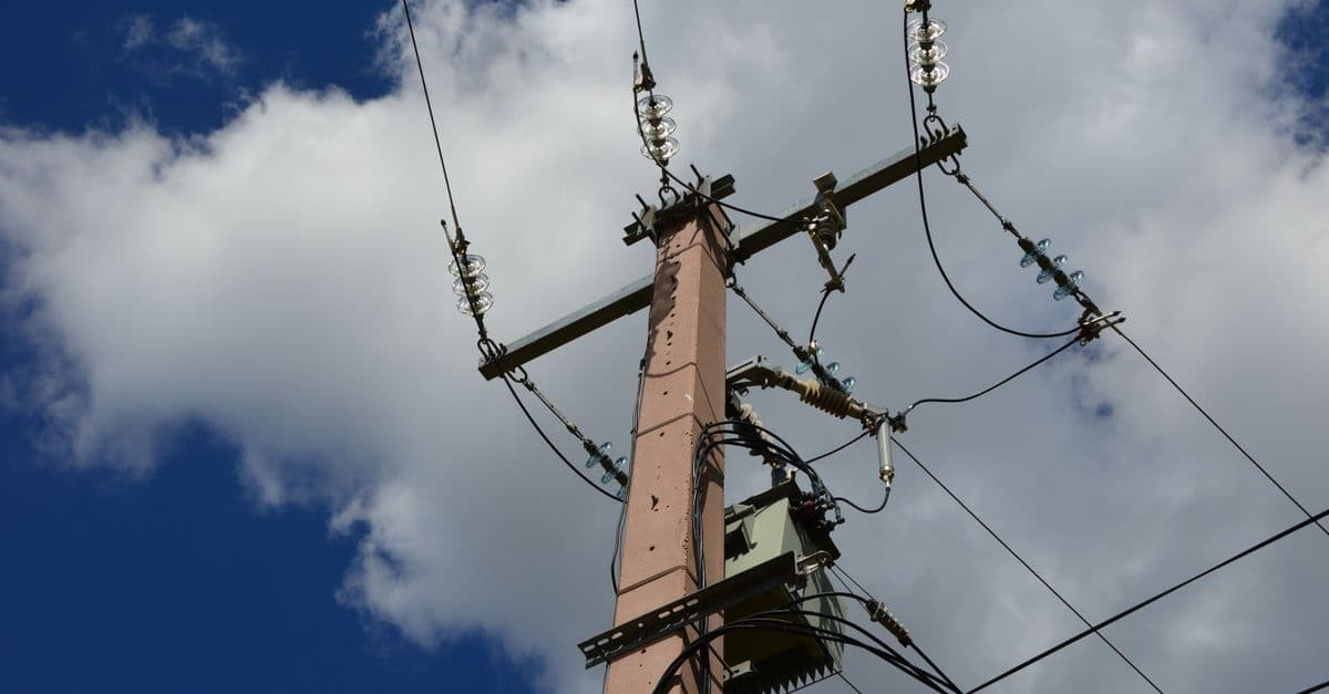 Low-angle view of a utility pole and power lines set against a blue sky with white clouds.