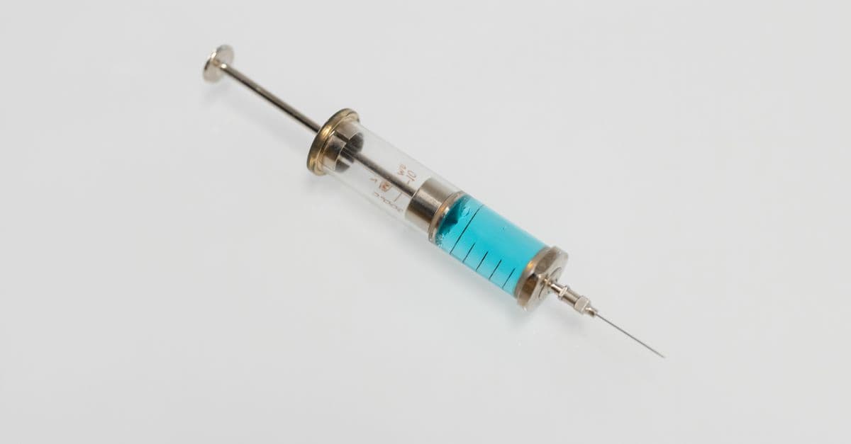 Close-up of a vintage glass syringe filled with blue liquid on a white background, minimal healthcare concept.