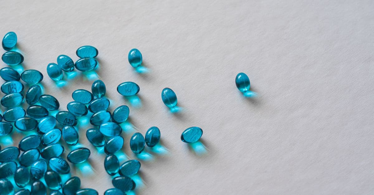 High angle view of scattered blue gel capsules on a flat white surface.