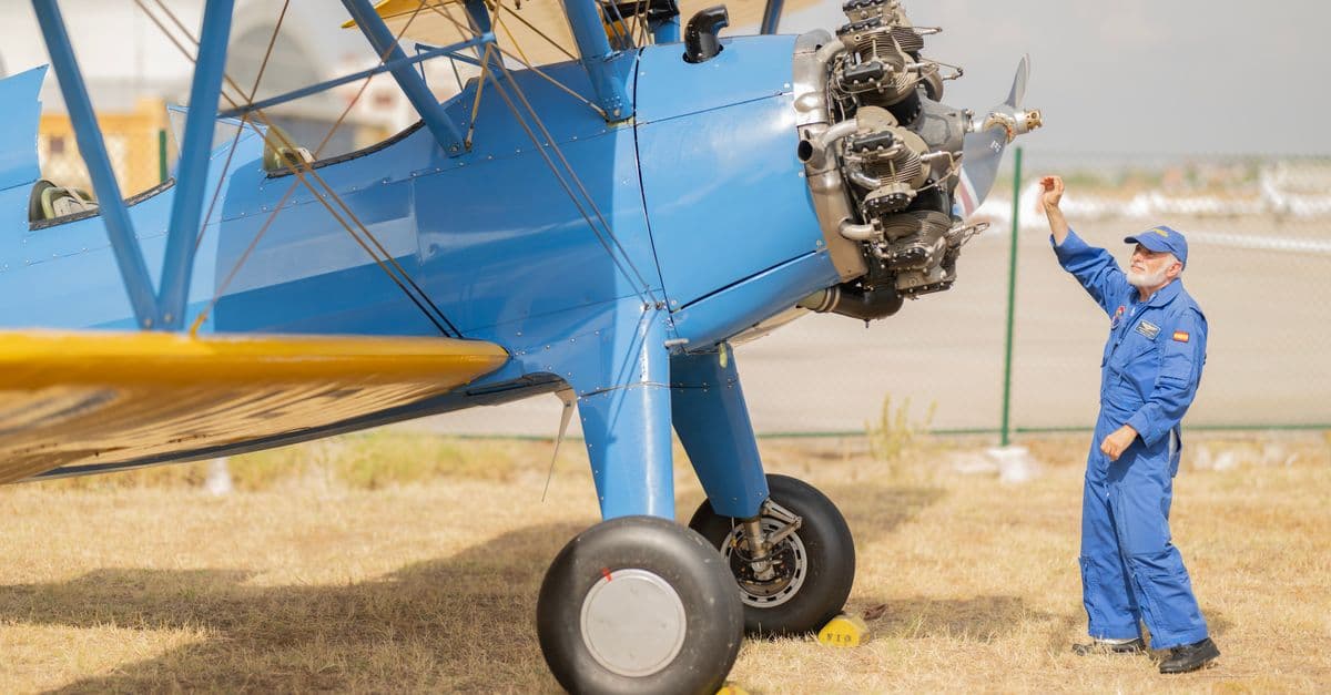 A mechanic checks a vintage biplane at an airfield in Madrid on a sunny day.