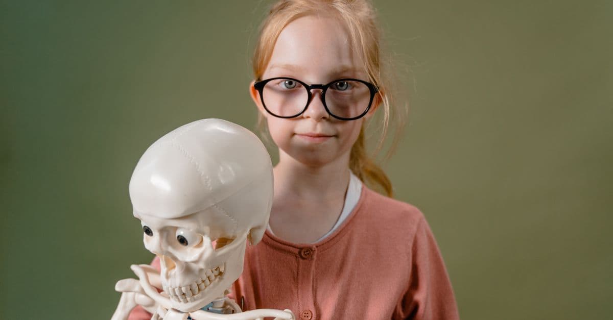 Young girl with glasses holding a plastic skeleton model, educational concept.