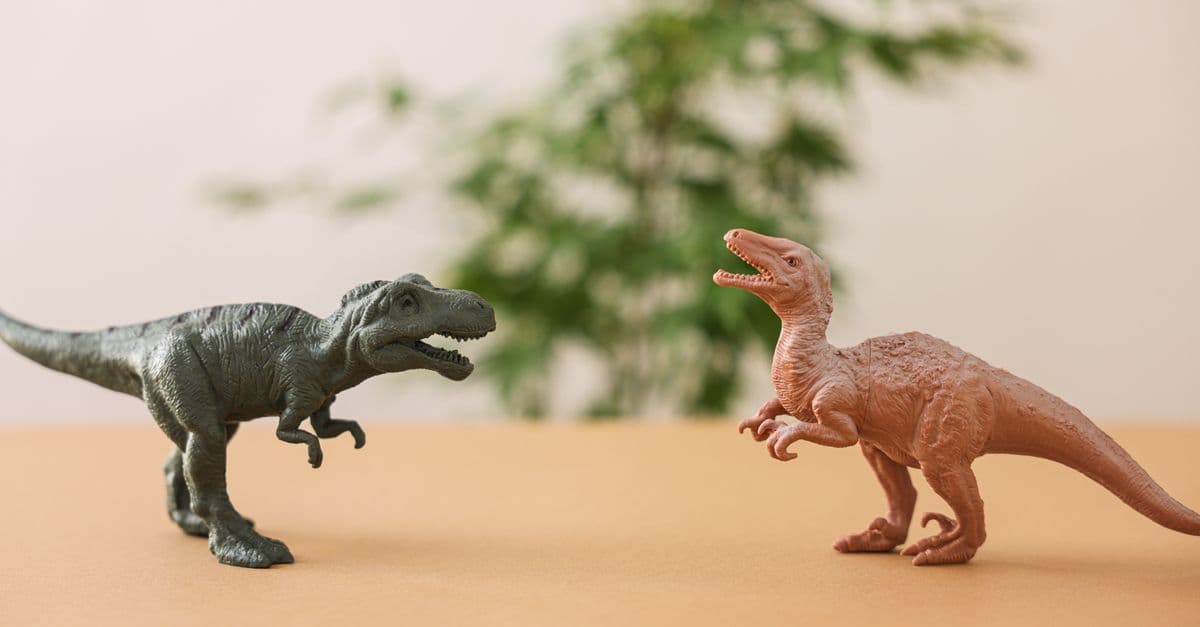Two toy dinosaur figures set against a natural background on a table.