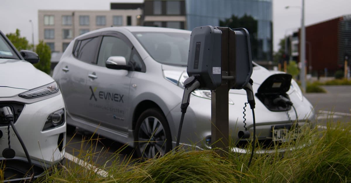 Electric vehicles at a charging station in Christchurch parking lot with modern architecture.