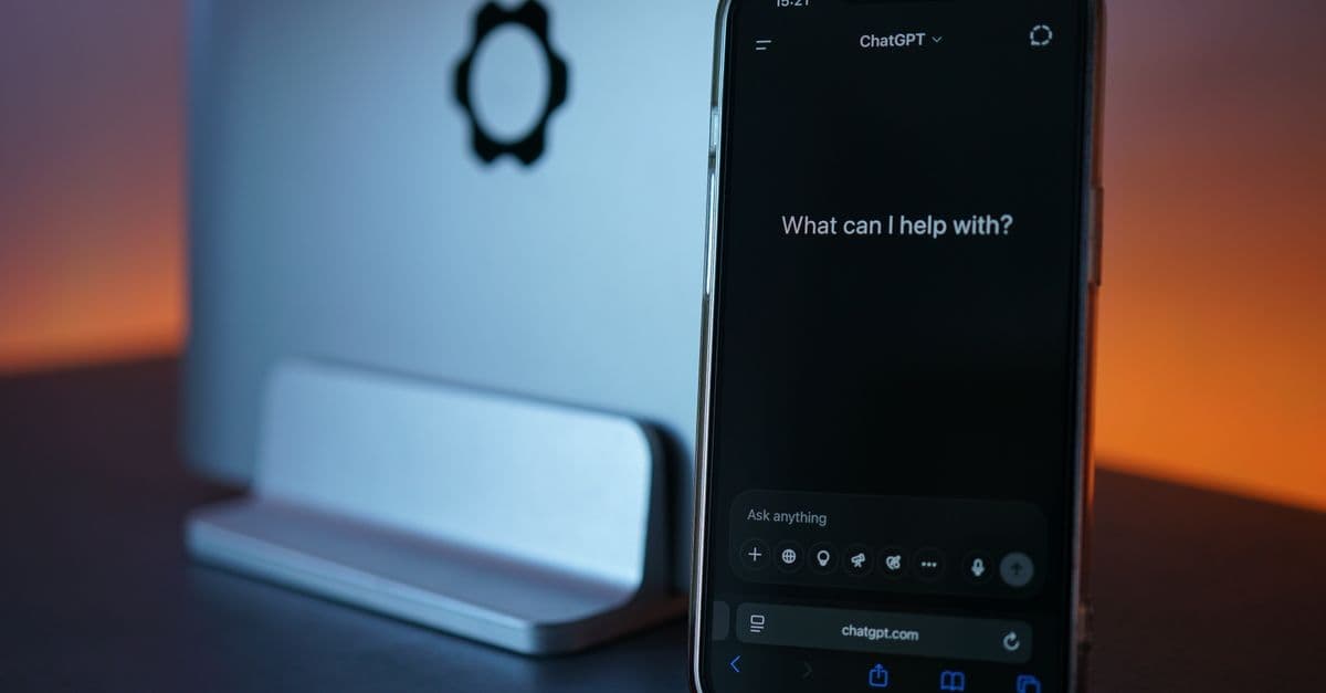 Close-up of a smartphone showing a chat interface with a laptop in the background.