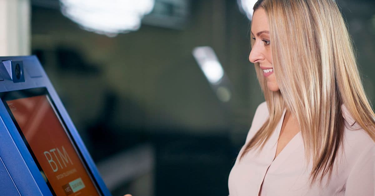 A woman interacts with a modern digital ATM for cryptocurrency transactions in an indoor setting.