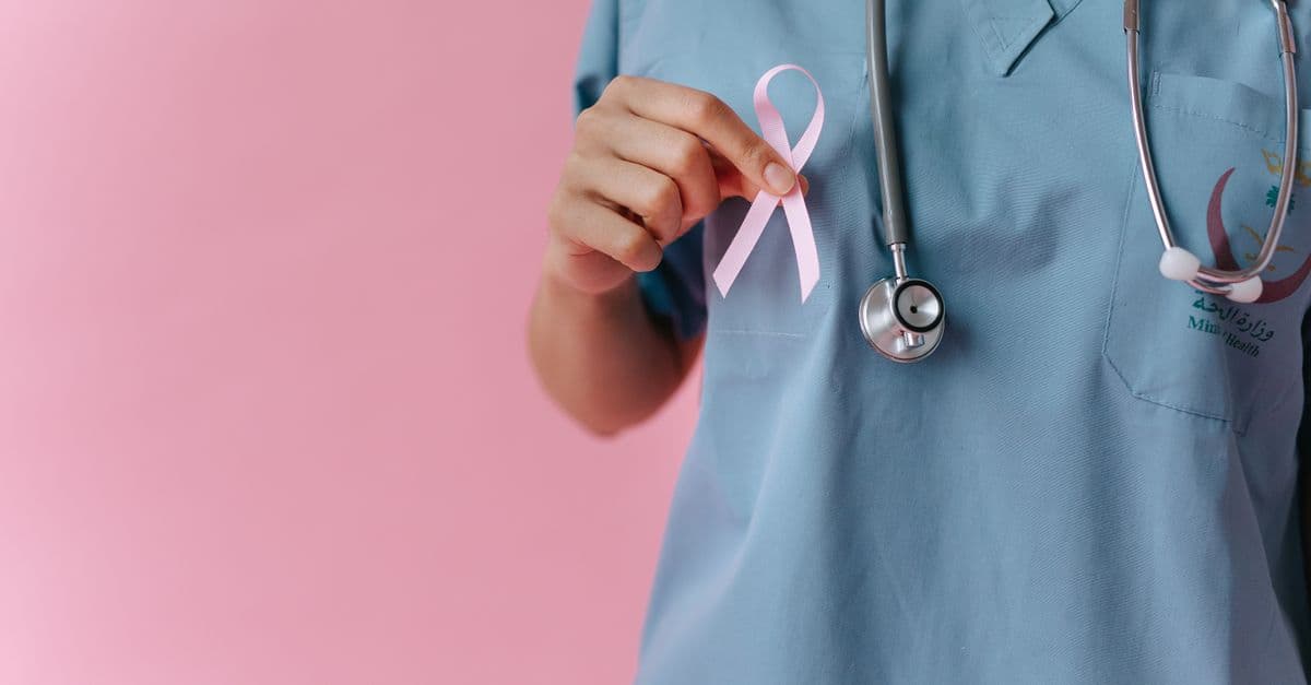 Healthcare worker in scrubs holds a pink breast cancer awareness ribbon symbolizing support.