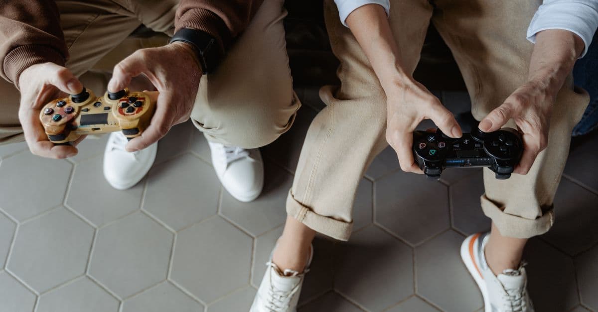 Two adults playing video games with controllers while seated on a sofa, having fun indoors.