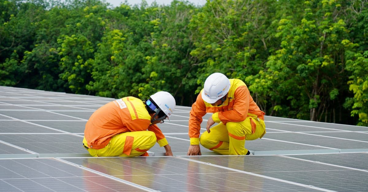 Workers installing photovoltaic solar panels on a sunny day, promoting renewable energy.