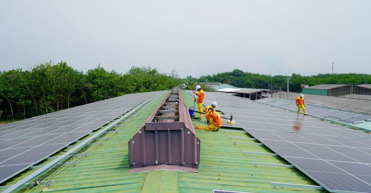 Team installing solar panels on a large rooftop under a clear sky, promoting renewable energy.