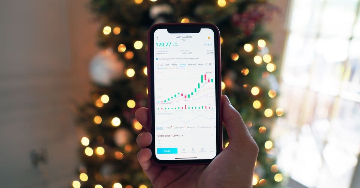 Close-up of a smartphone displaying stock market trading app with a background of Christmas lights.
