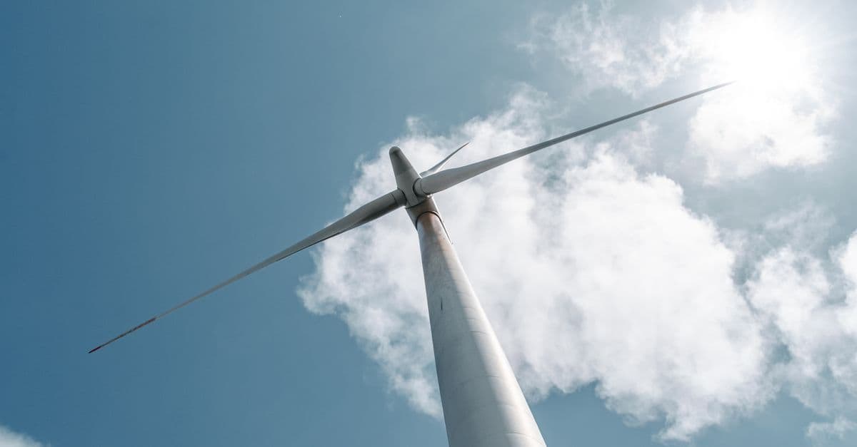 Low-angle view of a wind turbine with sunlight and clouds in the sky.