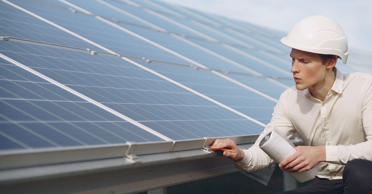 Focused young male employer in formal wear and hardhat working on solar panel station and checking details of modules