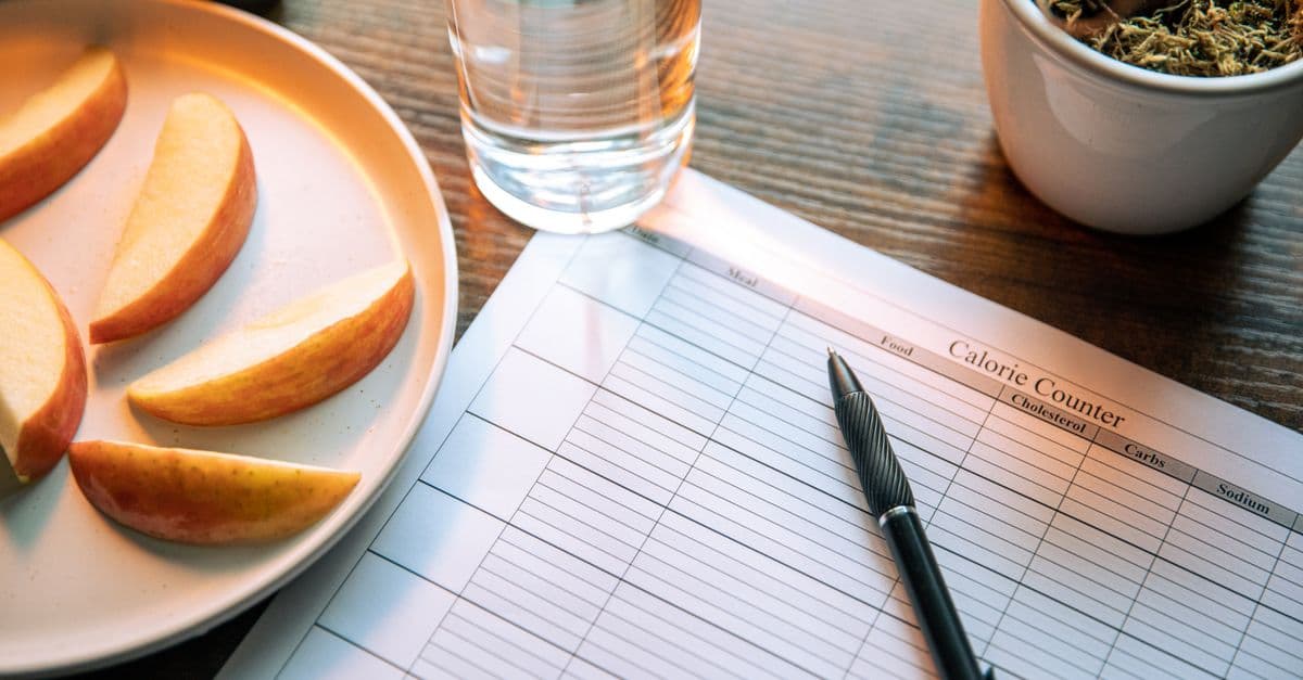 Flat lay featuring apple slices, a calorie counter chart, pen, and a glass of water for a healthy lifestyle.