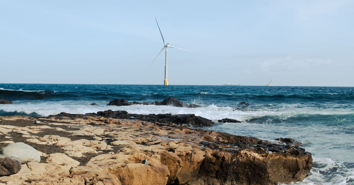 Wind turbine overlooking a rocky coastline with waves, showcasing renewable energy by the sea.