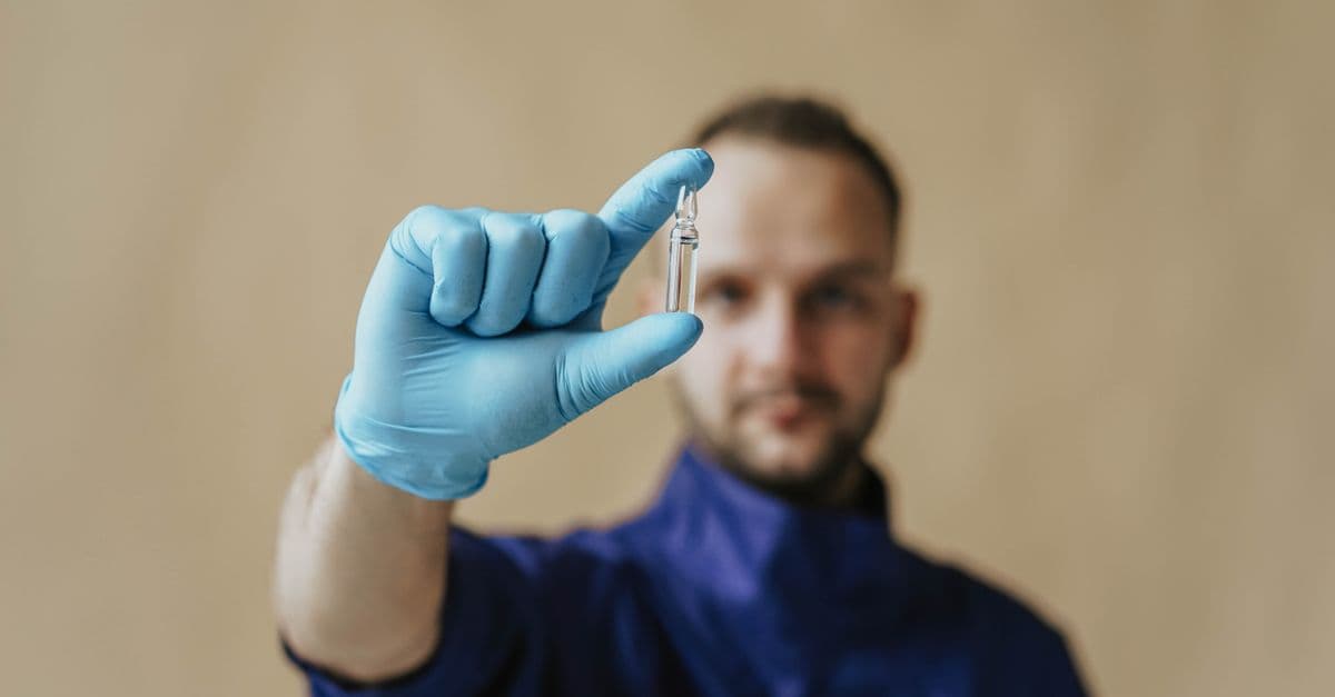 A male healthcare worker in protective gloves holding a small vial, focusing on medical research and safety.