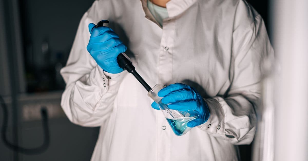Scientist in a lab coat using equipment for a chemical experiment.